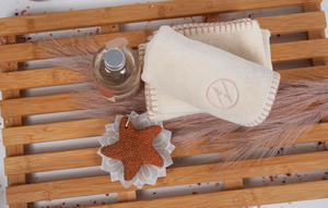 Natural color washcloths rolled up on a wooden slatted board next to a starfish, and a small bottole of soap.