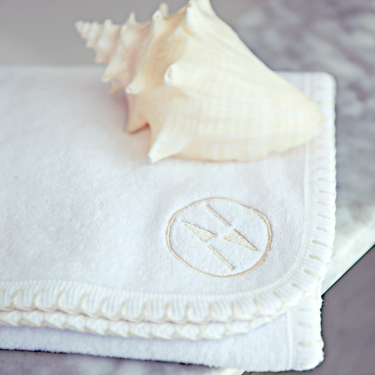 Close up of a white nautical themed washcloth with a sea shell resting on top.
