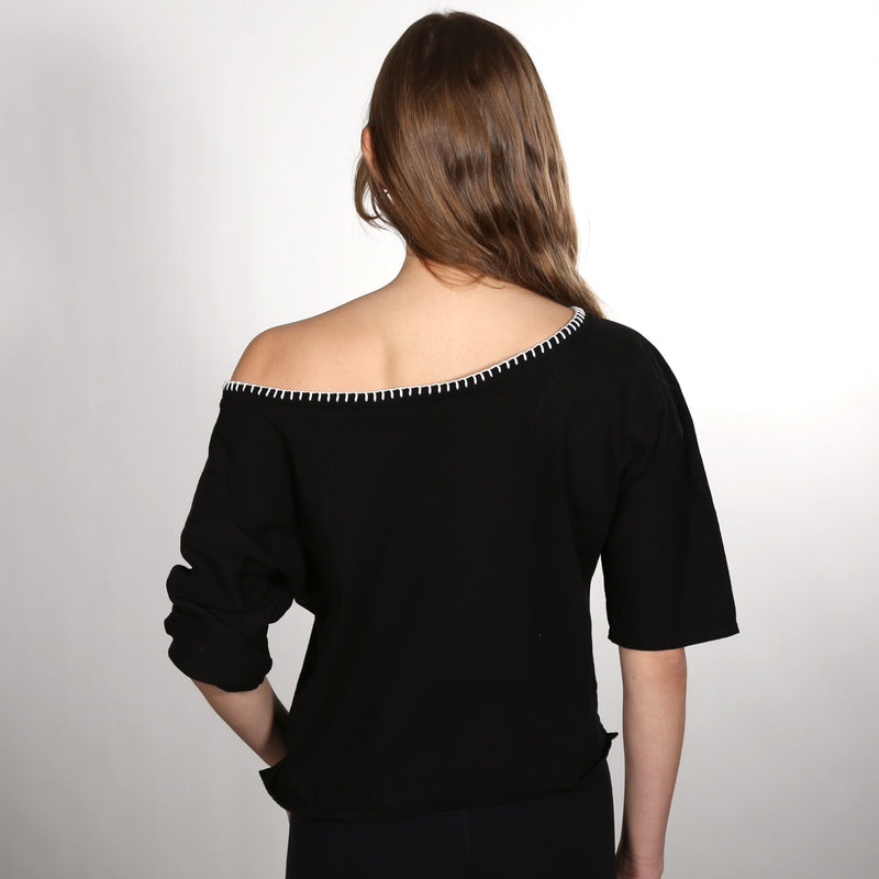 Woman with her back to the camera wearing a black wide neck nautical themed T Shirt on a white background
