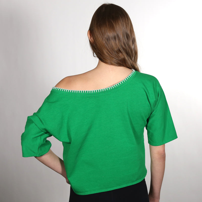 Woman with her back to the camera wearing a green wide neck nautical themed T shirt on a white background.