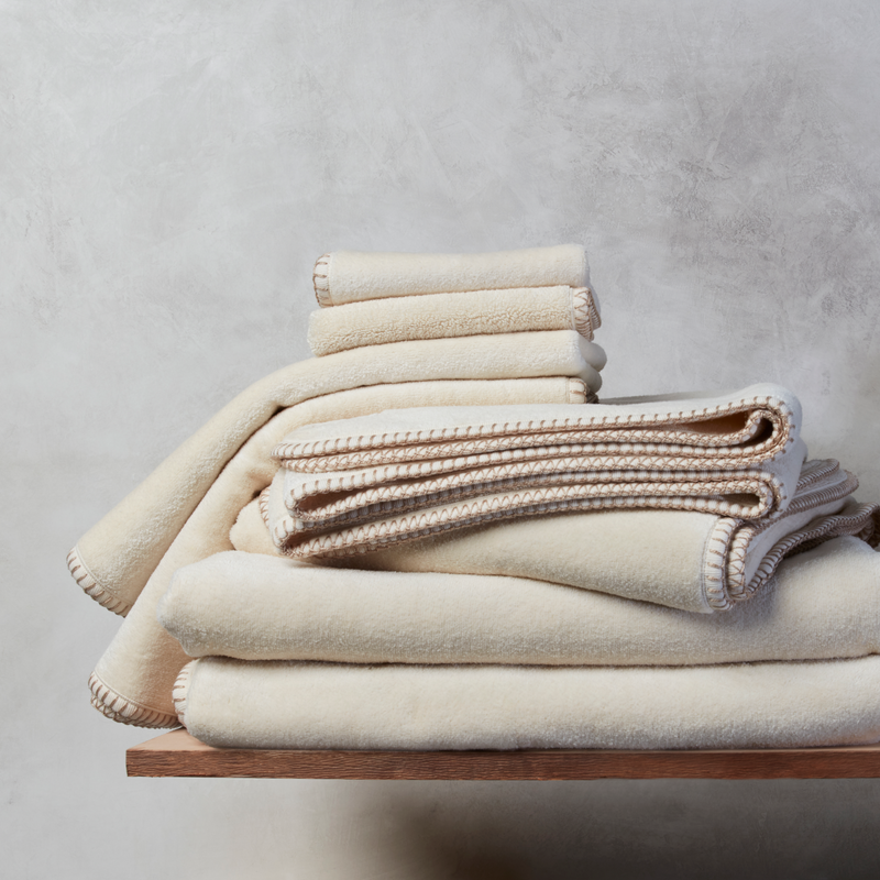 A stack of champagne colored nautical themed towels on a wooden plank against a grey background