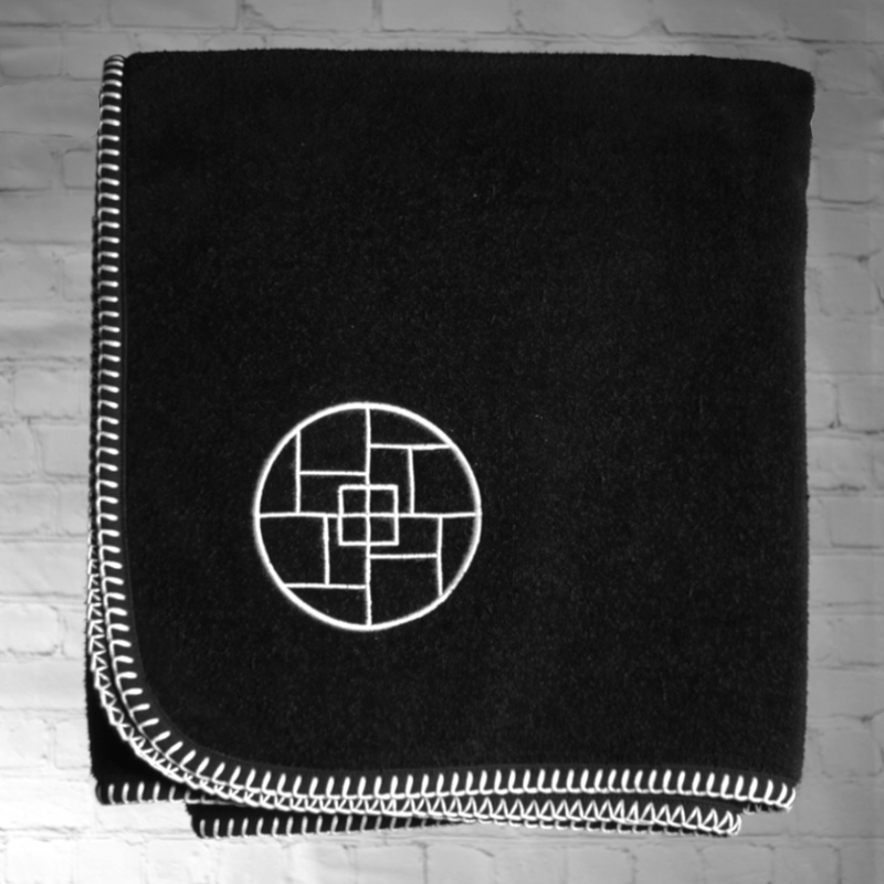 A nautical themed black towel with white edge stitching and a circle with squares within the circle embroidered on the towel.