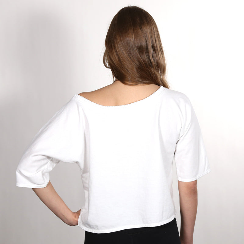 Woman with her back to the camera wearing a white wide neck nautical themed T Shirt on a white background