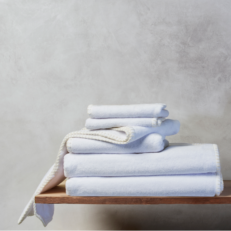 Stack of nautical themed white Bath, Hand, and Wash towels resting on a wooden shelf with a grey background
