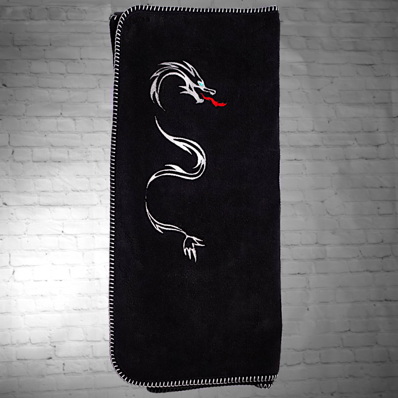 A wide view of the whole nautical themed black towel with white edge stitch and a dragon embroidered on it.