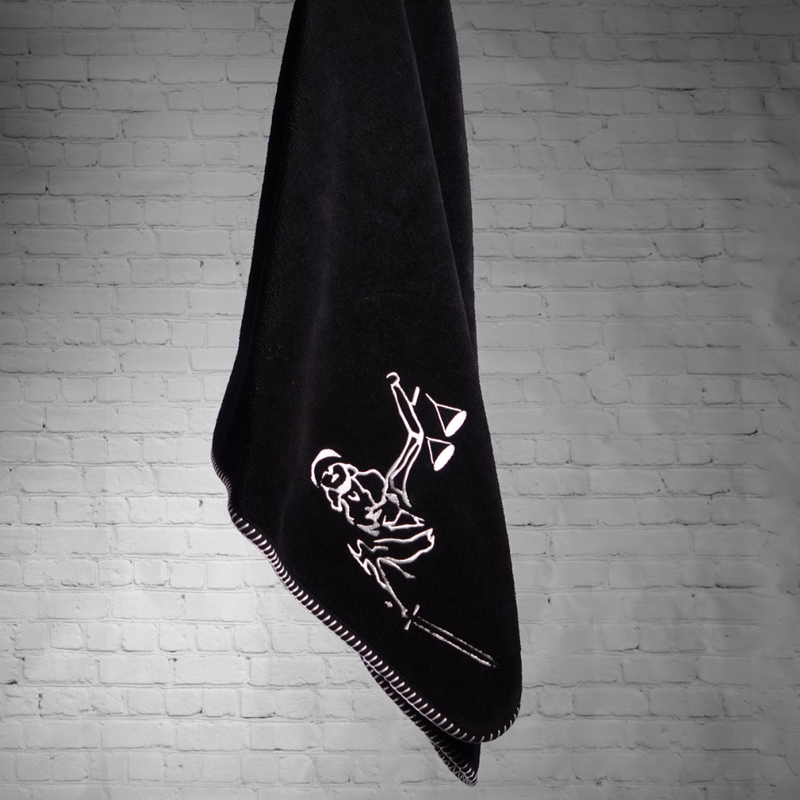 A black nautical themed towel with white stitching with Lady justice embroidered on it, hanging.