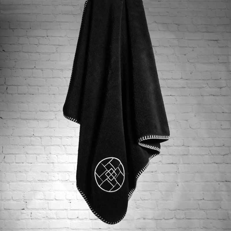 A nautical themed black towel with white edge stitching and an image of a circle with squares in it embroidered on the towel