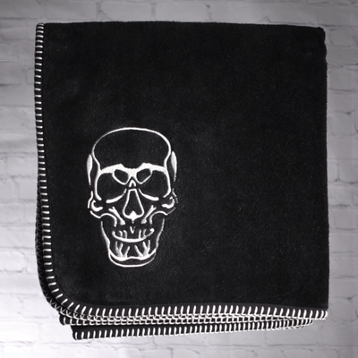 A nautical themed black towel with white edge stitching and an image of a skull embroidered on the towel.