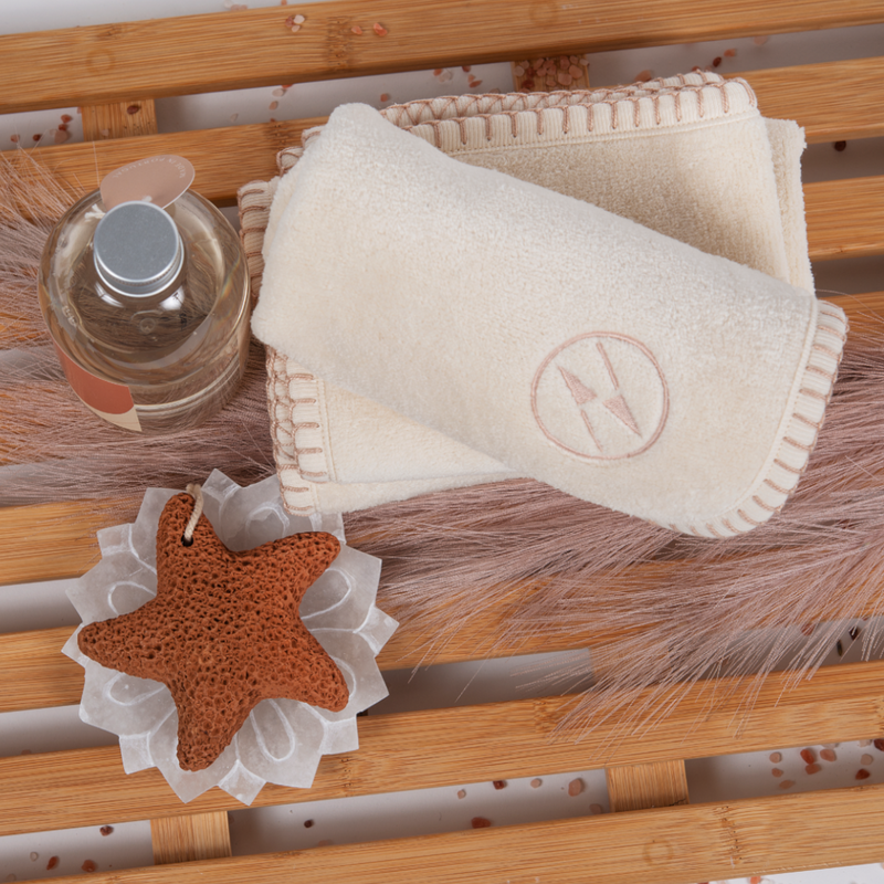 Champagne color nautical themed washcloths rolled and folded on a wooden slatted board next to a starfish and a bottle of soap.